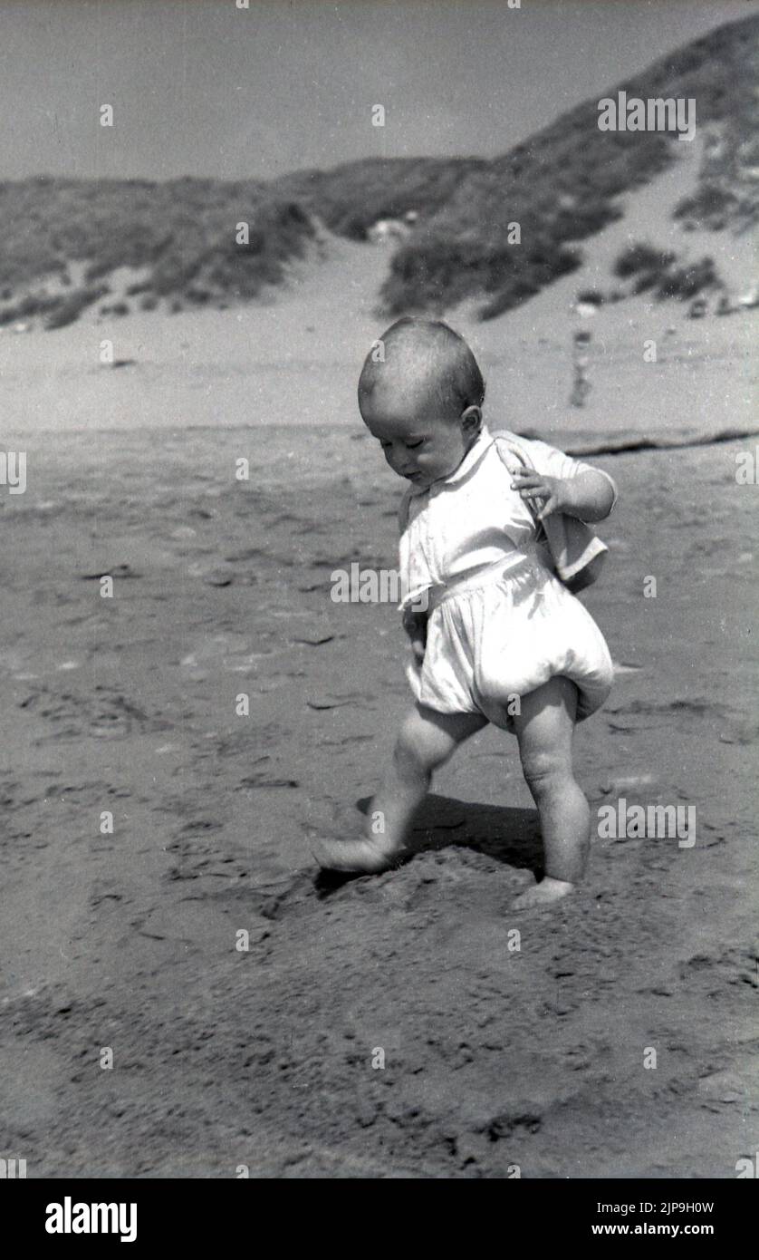 1950, historique, enfant en bas âge se fait une première expérience de marche sur sa propre plage de sable Angleterre, Royaume-Uni. Banque D'Images
