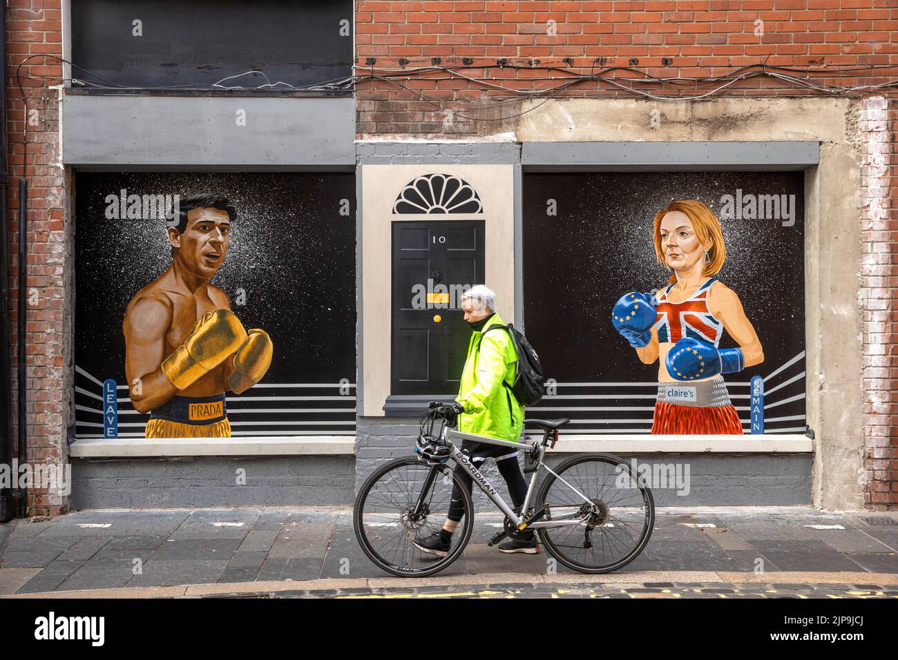 Une femme passe devant une fresque sur Hill Street à Belfast par Ciaran Gallagher Art, commandée par le propriétaire du bar local Willie Jack, montrant les candidats conservateurs du parti, Rishi Sunak et Liz Truss comme deux boxeurs sur le point de se battre pour devenir le premier ministre du Royaume-Uni. Date de la photo: Mardi 16 août 2022. Banque D'Images