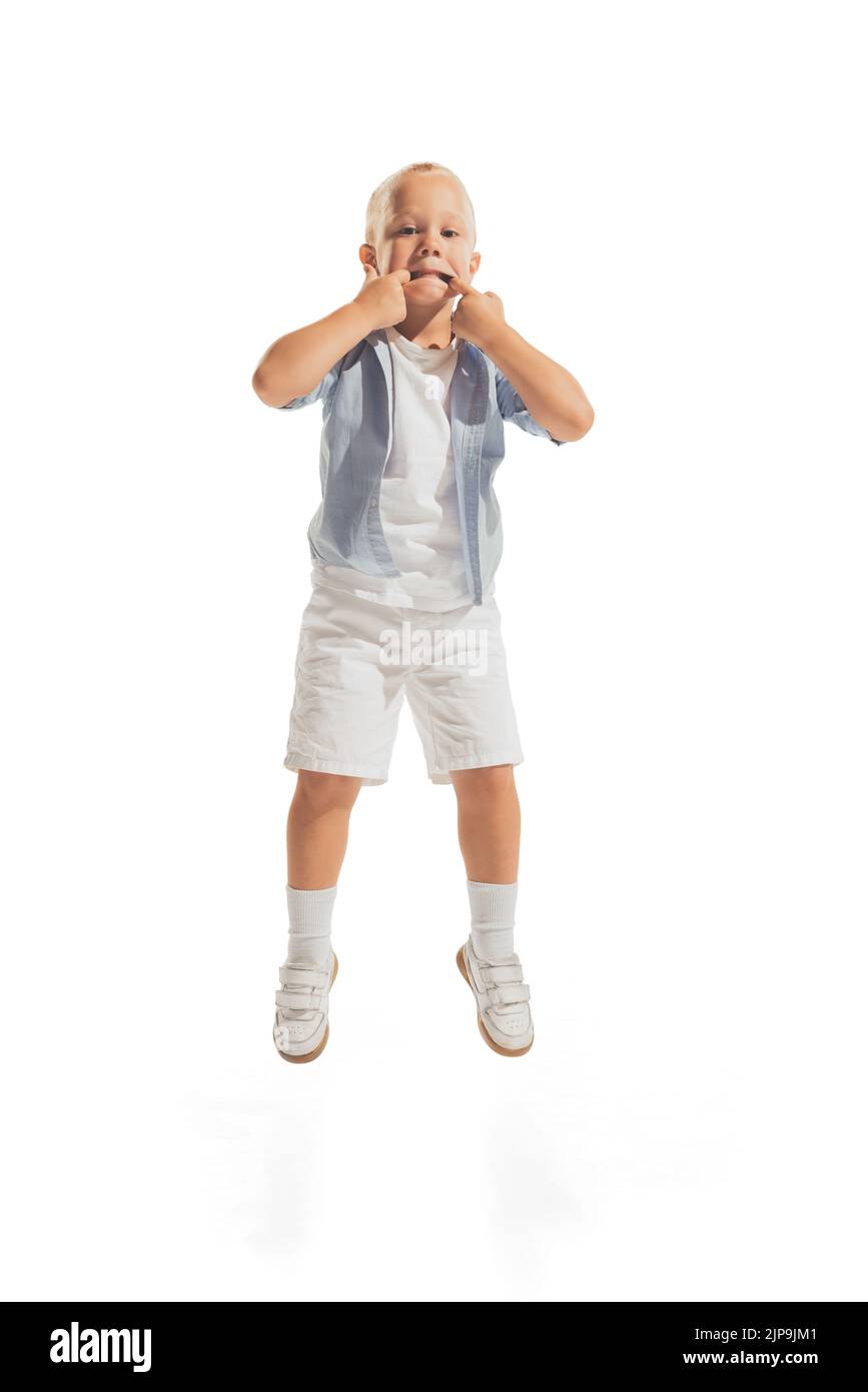 Portrait de petit garçon, enfant dans une tenue décontractée posant, faisant des visages drôles isolés sur fond blanc de studio Banque D'Images