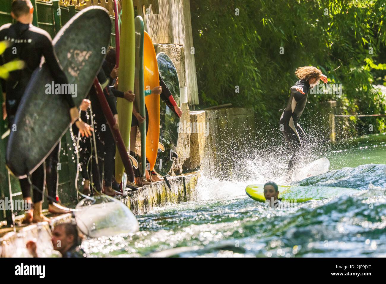 16 août 2022, Bavière, Munich: Les surfeurs avec leurs planches colorées attendent leur occasion de monter une vague artificielle dans le jardin anglais, au coeur de la capitale bavaroise. Photo: Peter Kneffel/dpa Banque D'Images