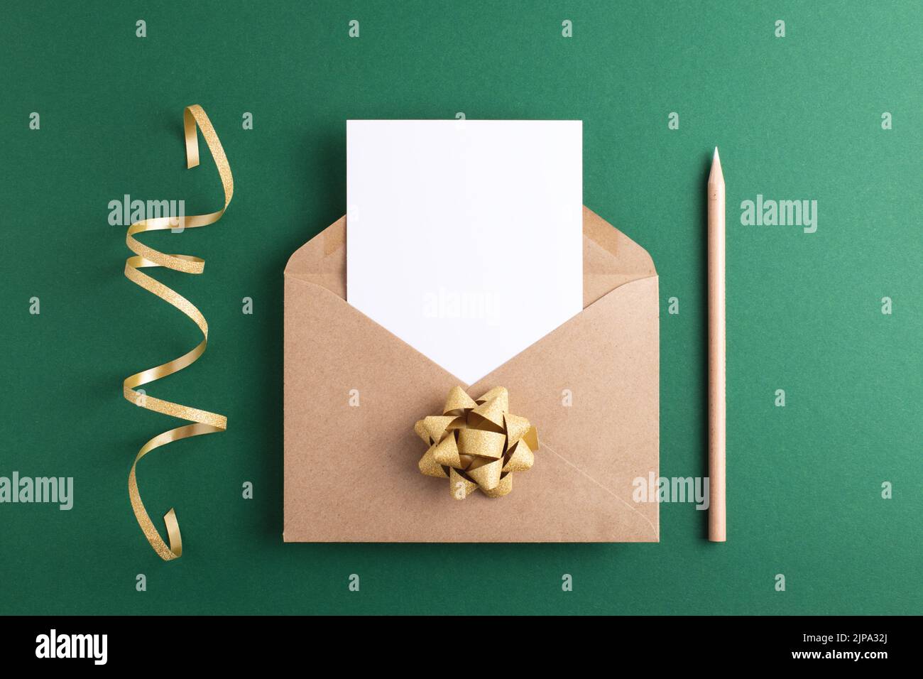 Carte vide dans une enveloppe de fête, décorations dorées et crayon de bois sur fond vert. Maquette de vacances et d'invitation. Banque D'Images