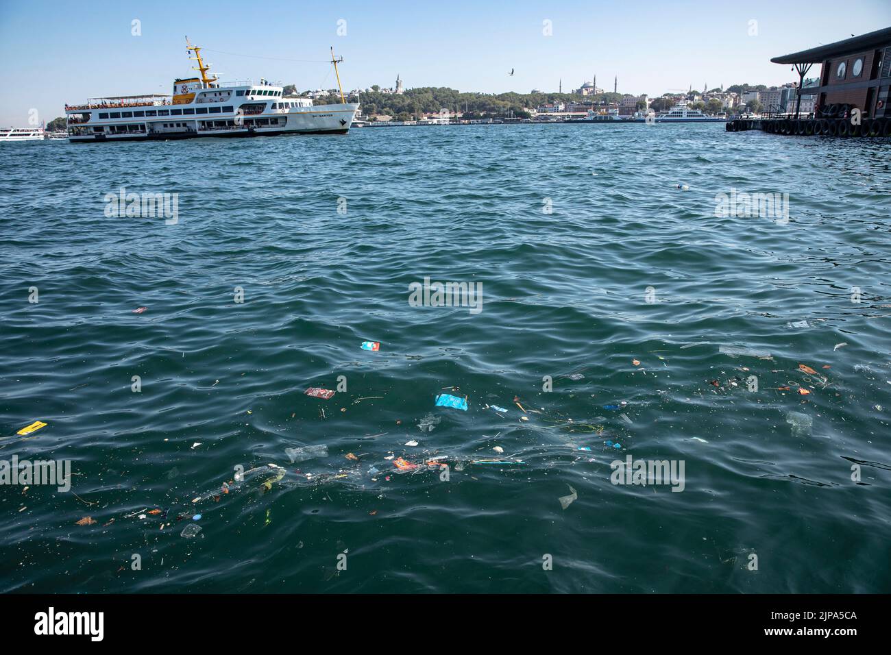 Le ferry des lignes de la ville et la mosquée Sainte-Sophie vu dans le fond des déchets plastiques jetables dérivant à la surface de la mer à l'intérieur et autour de la jetée des lignes de la ville de Karakoy suite à une forte pluie et une tempête à Istanbul. Banque D'Images