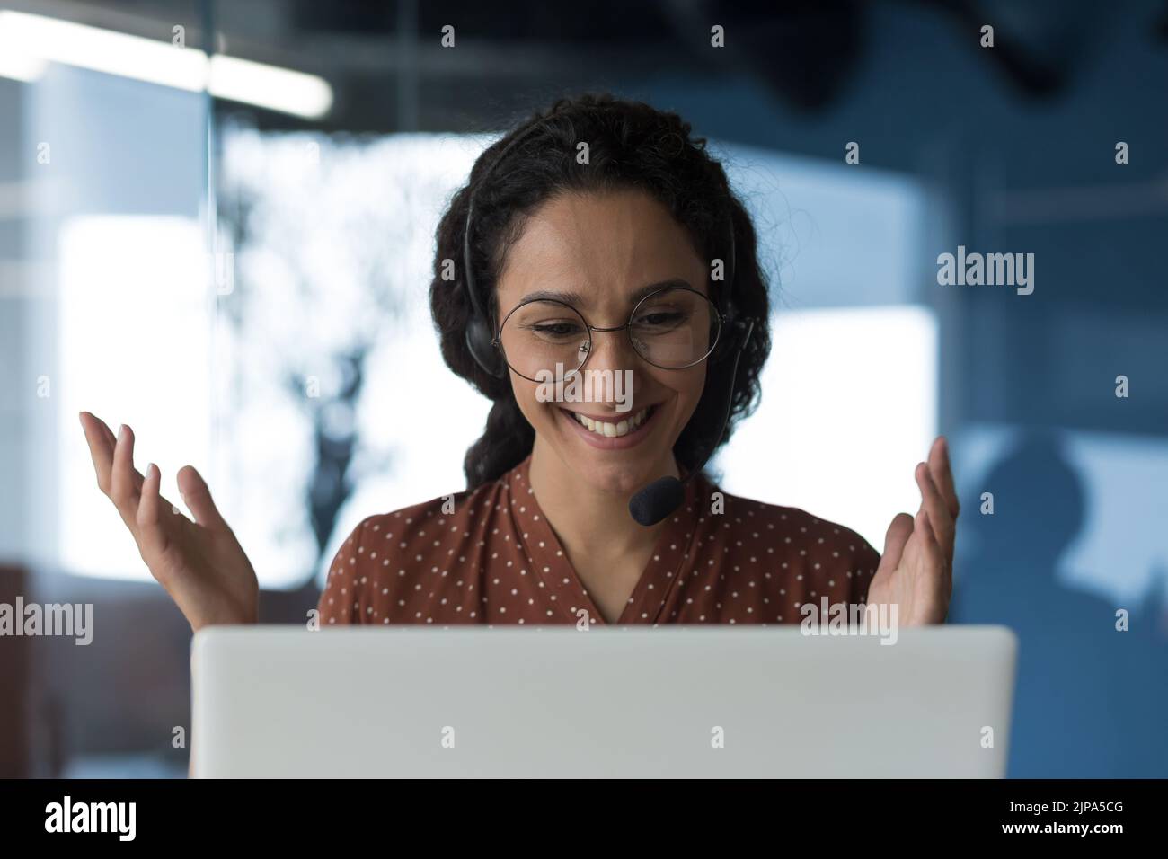 Photo en gros plan d'une jeune femme arabe en forme de curly qui parle lors d'un appel vidéo, regarde la webcam d'un ordinateur portable et sourit en utilisant un casque pour la communication, femme d'affaires prospère travaillant au bureau Banque D'Images