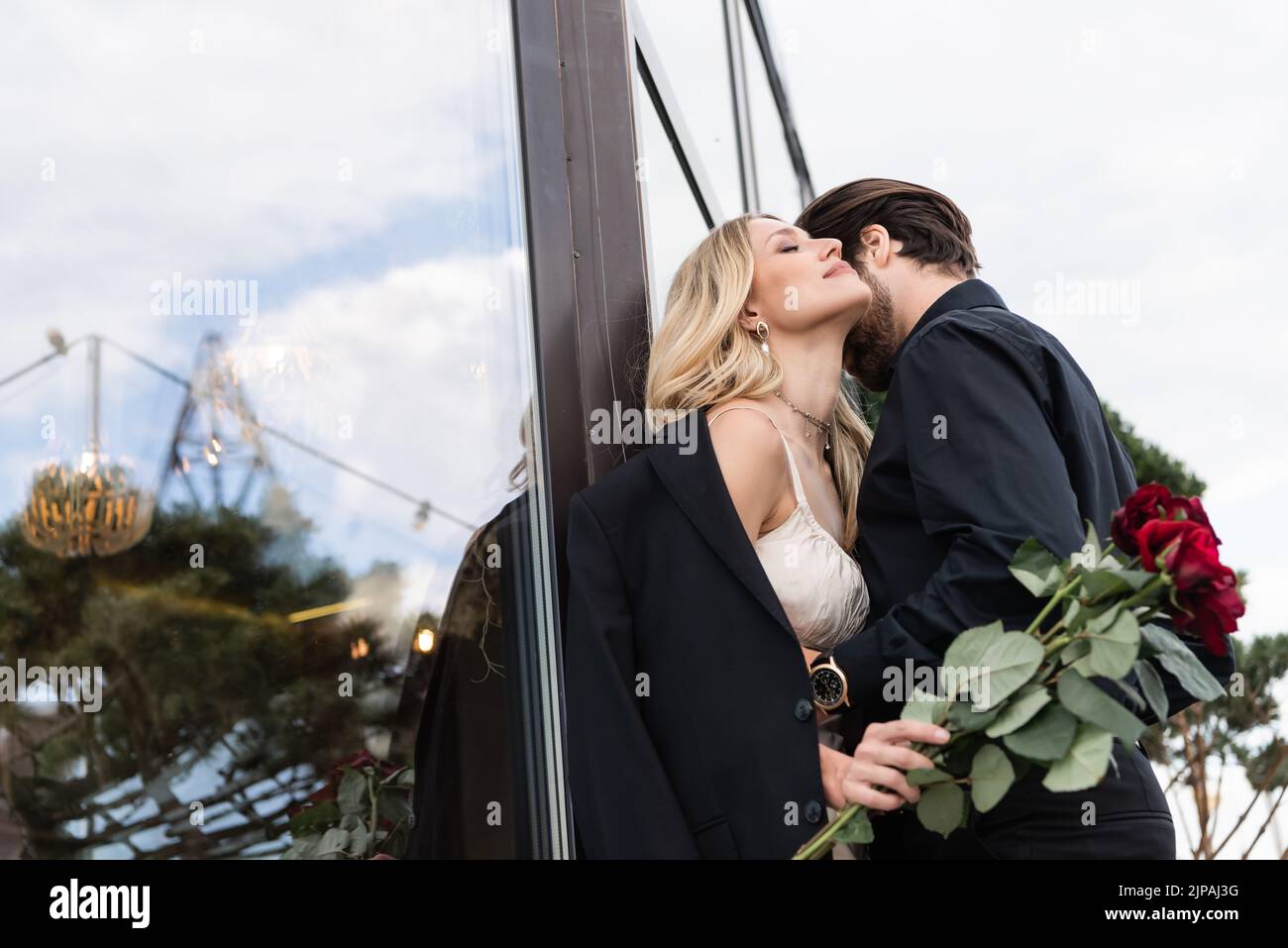 Jeune homme embrassant petite amie avec roses rouges sur la terrasse Banque D'Images