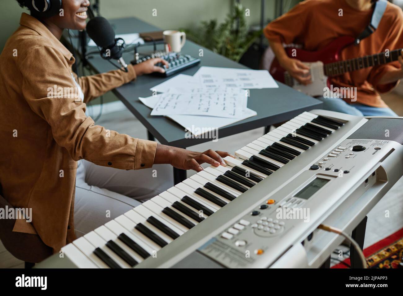 Gros plan de la jeune femme noire appuyant sur les touches du piano tout en composant de la musique avec un groupe de jeunes musiciens Banque D'Images