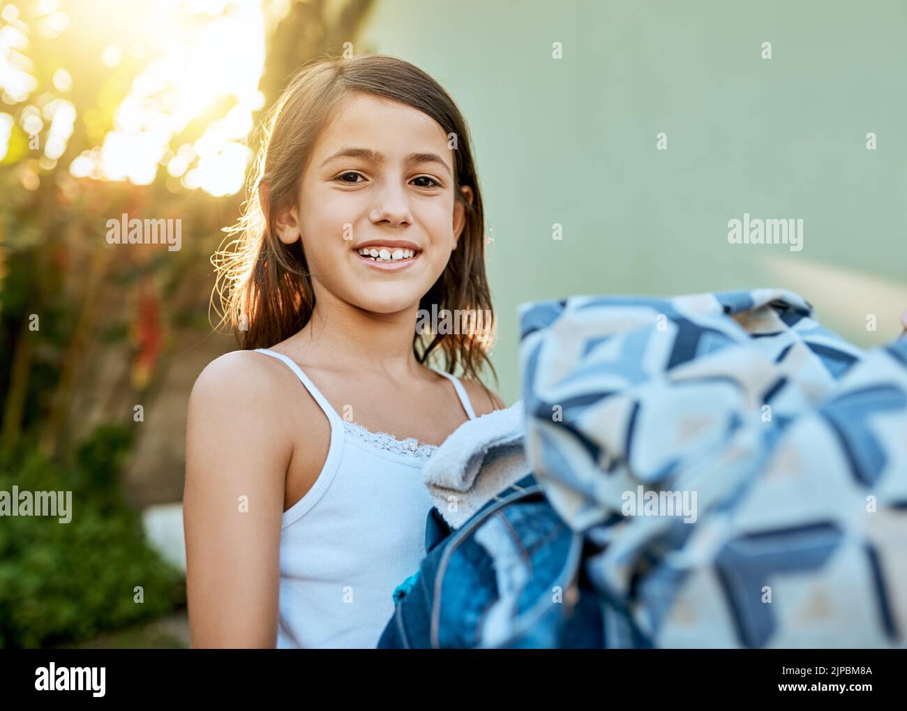 Regardez, je peux tout faire de la lessive par moi-même. Portrait d'une petite fille qui pendait le linge à l'extérieur. Banque D'Images