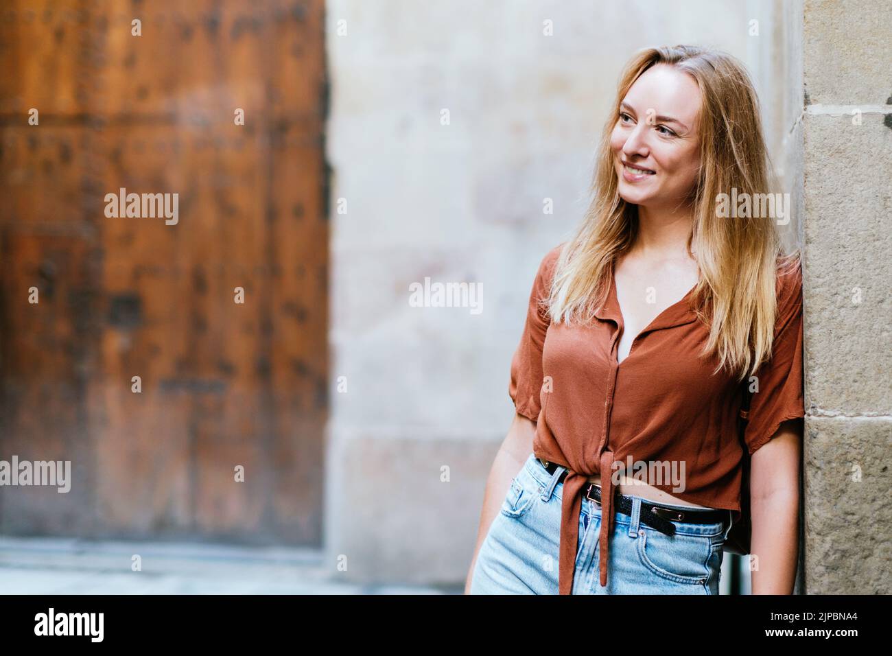Blonde blanche touriste penchée sur un mur de la vieille ville de Barcelone. Elle sourit et regarde d'un côté Banque D'Images