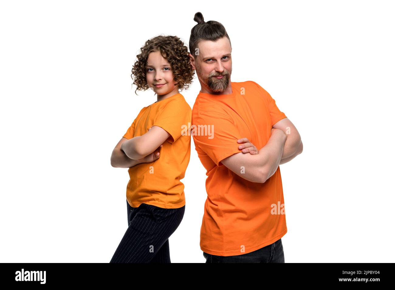 La jeune fille européenne à poil court 10-12s et le beau père barbu se tiennent dos à dos avec les bras croisés. Une famille heureuse porte des t-shirts orange de base Banque D'Images