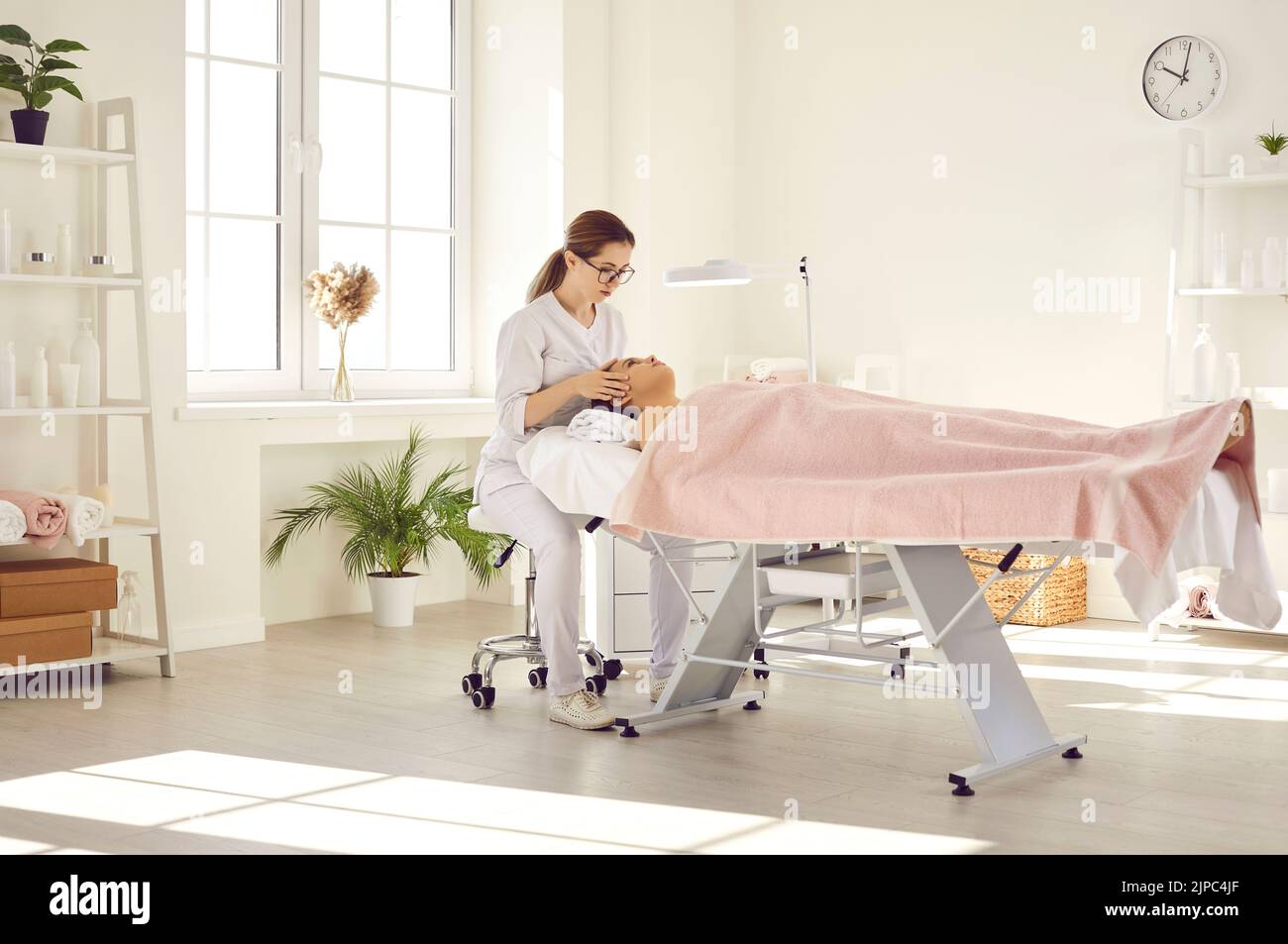 Une masseuse professionnelle féminine dans un salon de beauté fait un massage de son visage et de sa tête pour sa cliente féminine. Banque D'Images