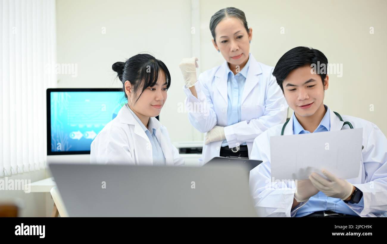 Deux jeunes scientifiques asiatiques ou techniciens médicaux travaillant, ayant une réunion de discussion médicale avec une femme asiatique supérieure superviseur scientifique dans le labo Banque D'Images