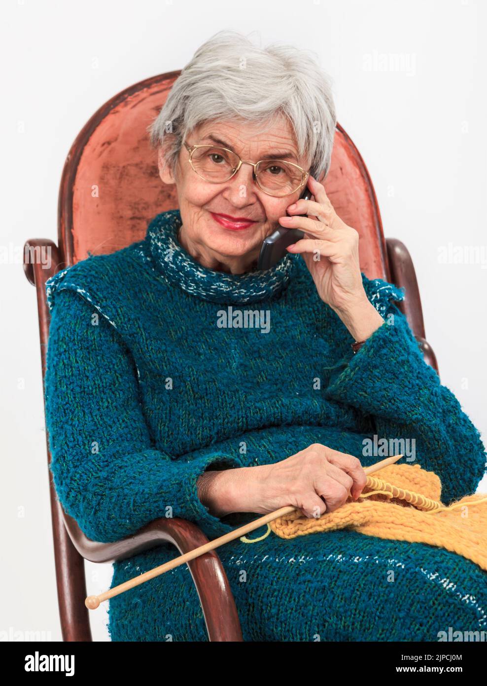 Portrait d'une femme âgée sur le mobile tout en étant assise dans un rocker tricotage. Banque D'Images
