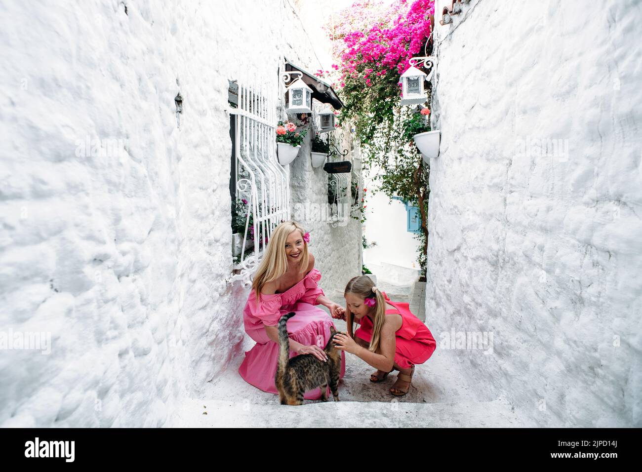 Femme d'âge moyen mère et fille adolescente blonde jouant avec un chat non domestique dans la rue médiévale de Marmaris, Turquie. Un parent Banque D'Images