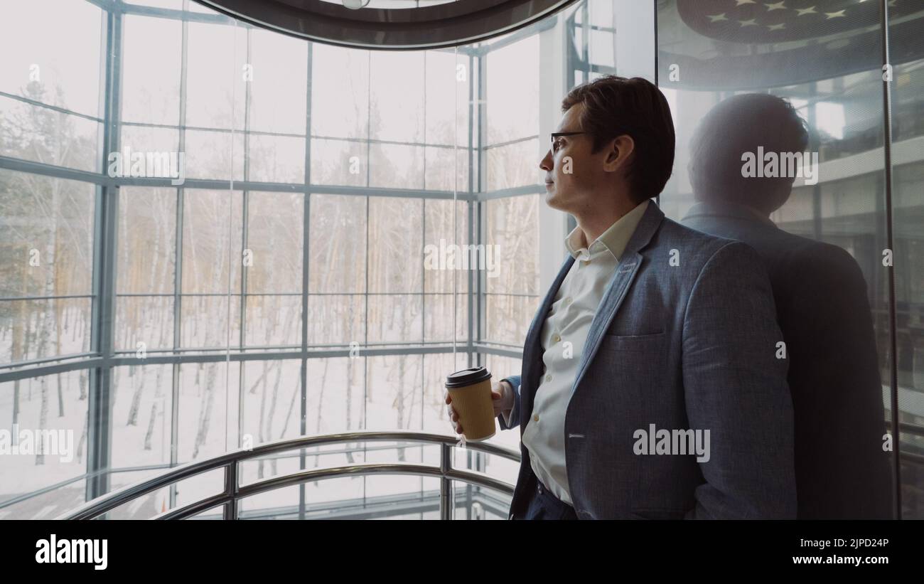 Jeune homme d'affaires élégant en costume buvant du café à l'intérieur d'un celeaviateur dans un centre d'affaires moderne à l'intérieur Banque D'Images