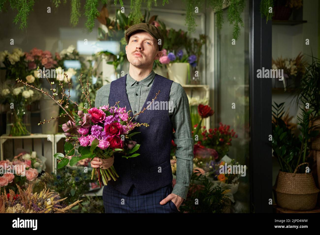 Grave émotion mâle caucasien en chapeau à pic et vêtements vintage de 20s tenant beau bouquet de fleurs rouges et violettes. Félicitez avec des fleurs. Concept de la fête des mères ou de la Saint-Valentin Banque D'Images