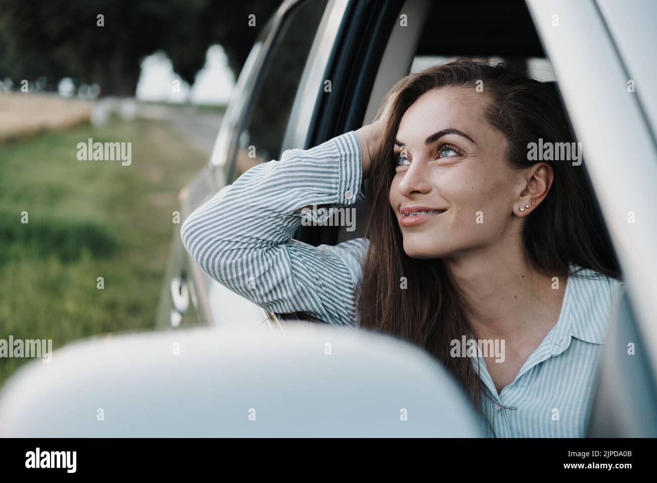 Cheeful femme caucasienne avec des bretelles appréciant le voyage de route et regardant dehors de la fenêtre de voiture Banque D'Images