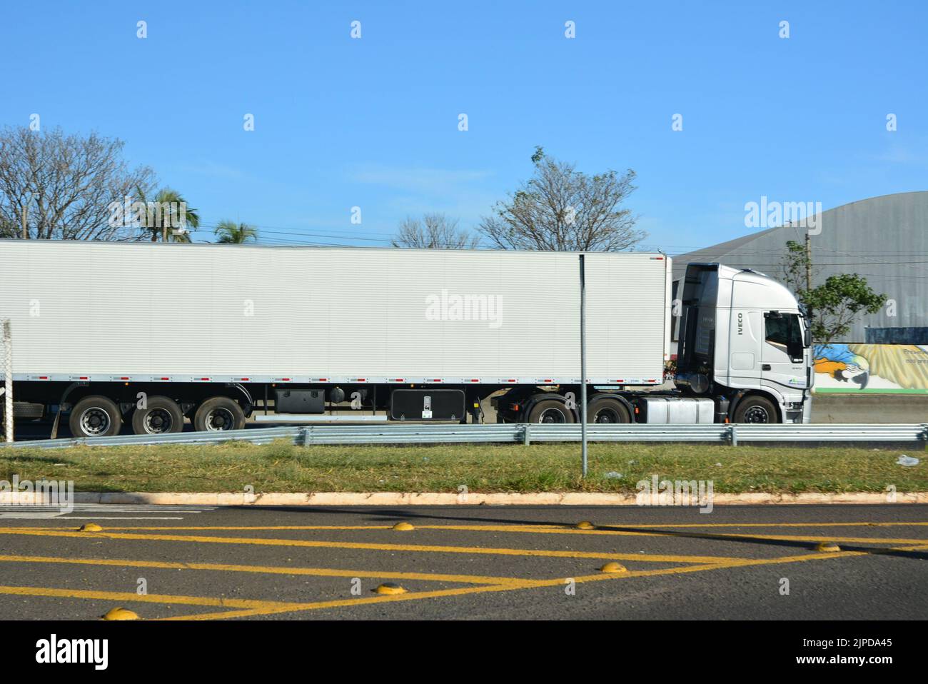 Camion de transport avec caisse métallique, autoroute brésilienne, vue latérale, arrière-plan avec flou intentionnel, avant-plan asphalte avec panneaux terrestres, autoroute en U. Banque D'Images