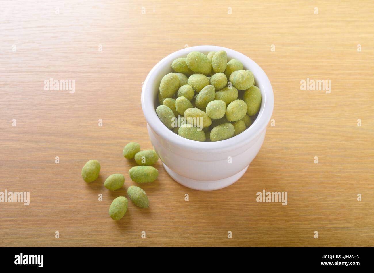 Bol de cacahuètes enrobées de wasabi sur table avec quelques noix et dispersés sur la table Banque D'Images