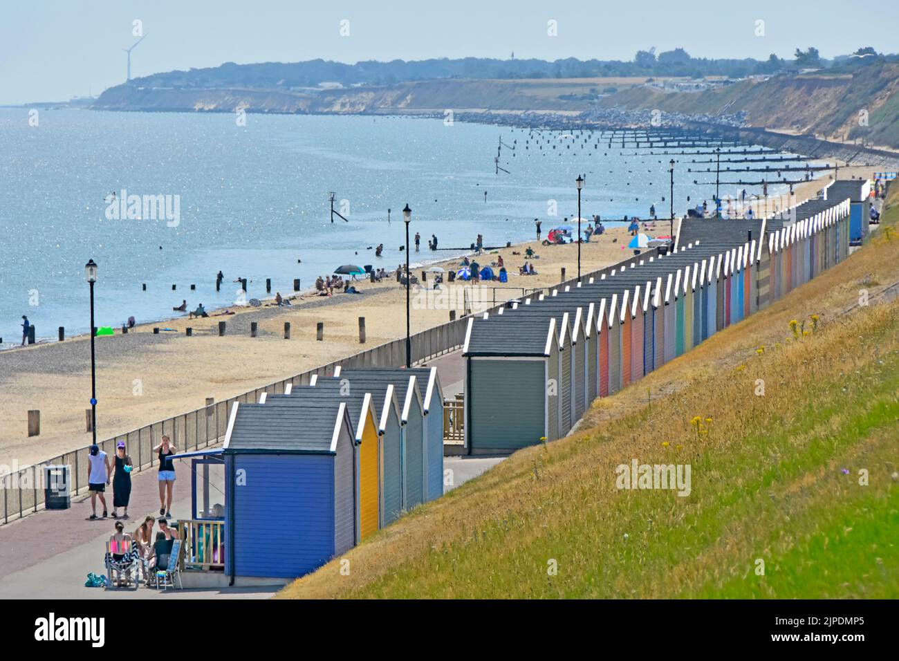 Station balnéaire de Gorleston-on-Sea et côte longue ligne de cabanes de plage sous les falaises d'herbe avec des groynes lointaines plus loin le long de la côte Norfolk Angleterre Royaume-Uni Banque D'Images