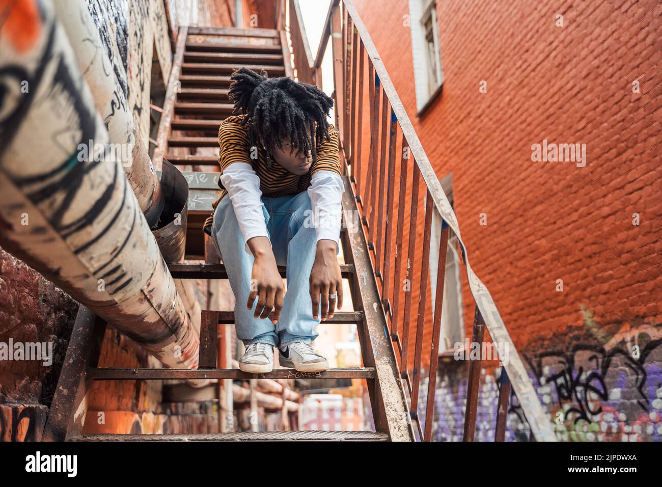 Jeune homme élégant noir avec des dreadlocks de cheveux naturels. Afroamerican Guy.Stairs, mur peint avec des graffitis dans le quartier pauvre de l'art de rue cultur Banque D'Images