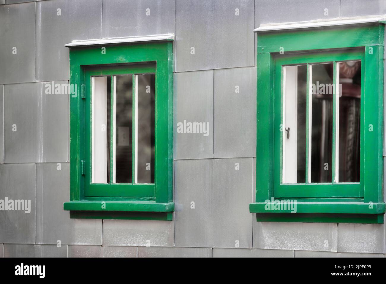Gros plan d'une fenêtre encadrée de vert sur un mur extérieur argenté. Banque D'Images Gros plan d'une fenêtre encadrée de vert sur un mur extérieur argenté. Banque D'Images