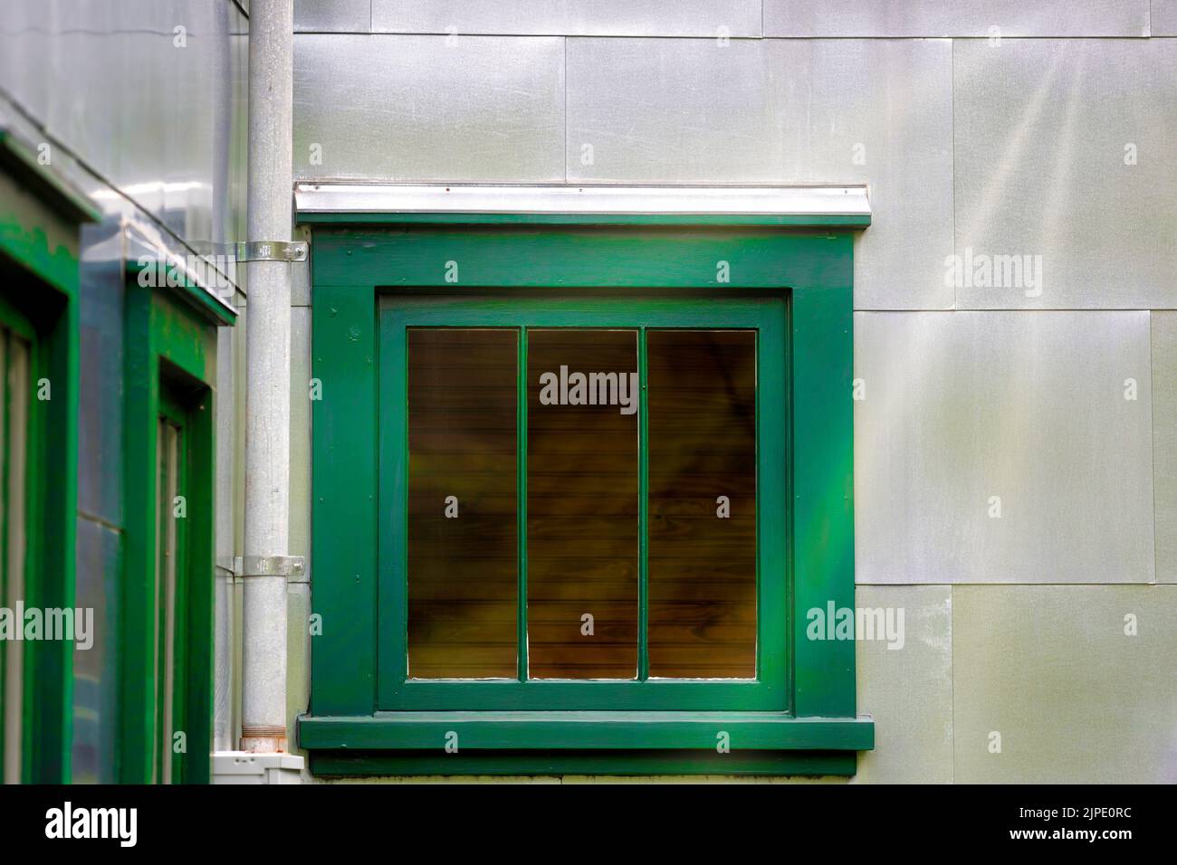 Gros plan d'une fenêtre encadrée de vert sur un mur extérieur argenté. Banque D'Images