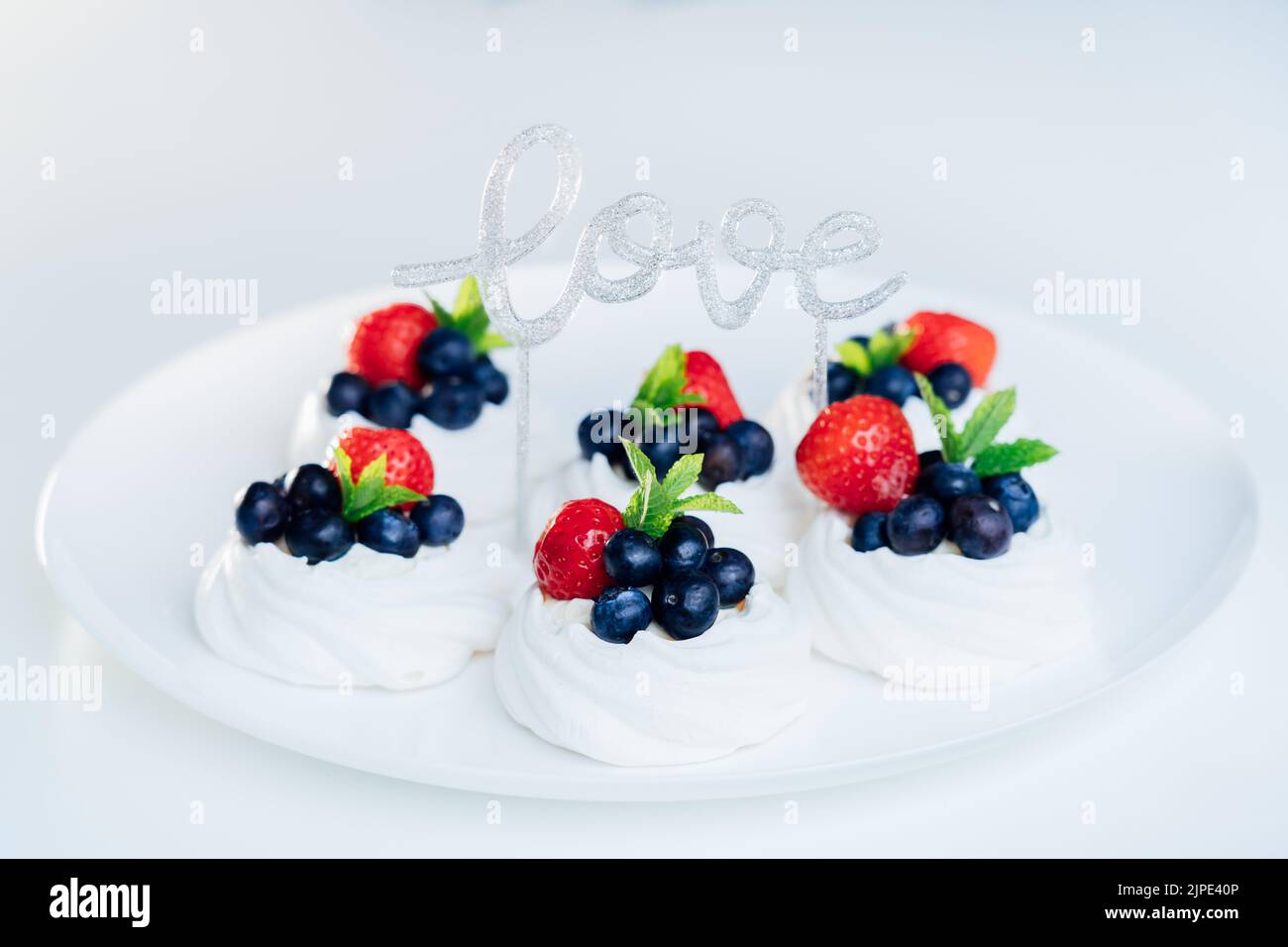 Dessert meringue gâteau Pavlova aux fraises fraîches et aux myrtilles avec menthe sur la plaque blanche et décor Love Word. Cadeau de Saint-Valentin Banque D'Images
