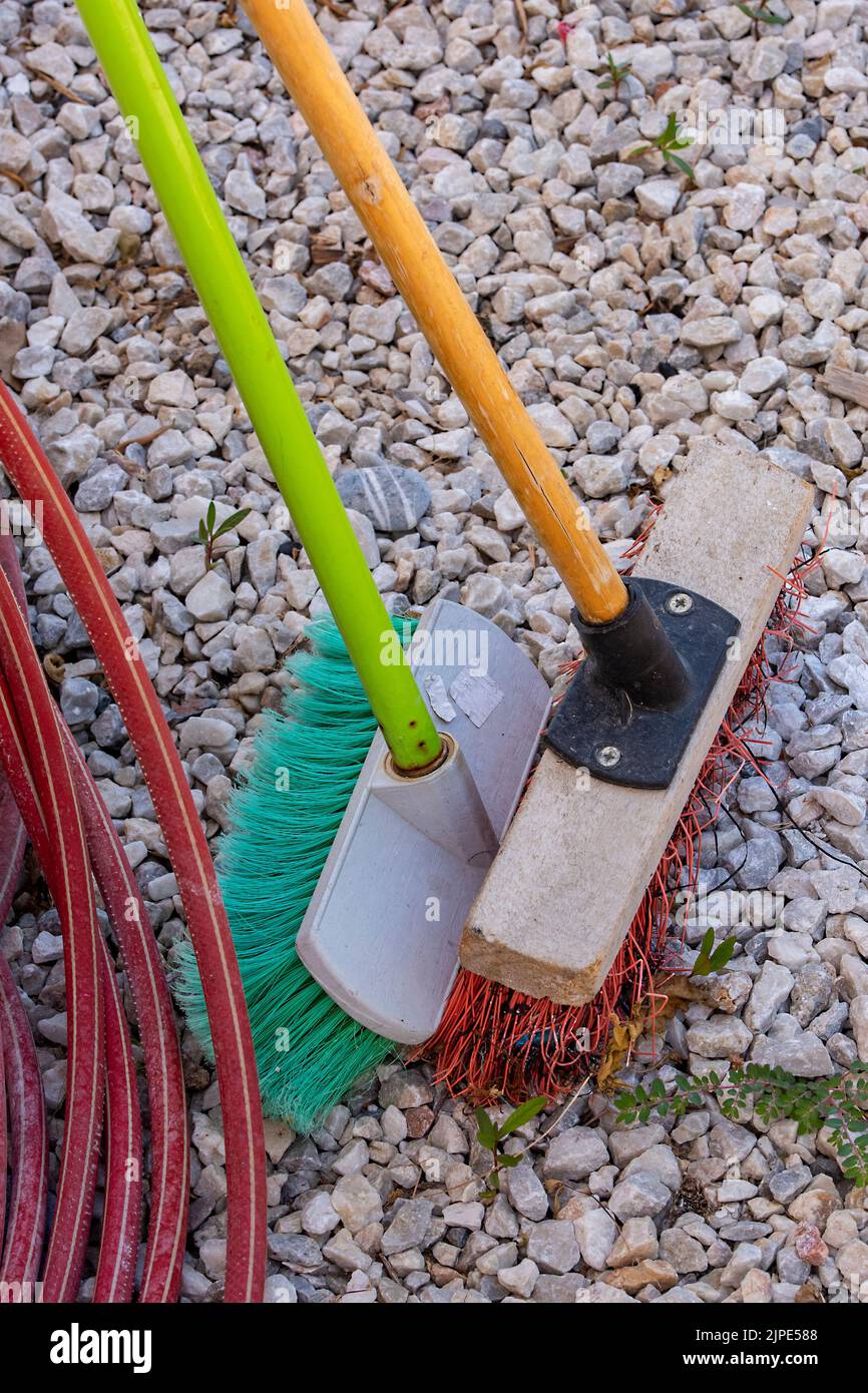 brosse à balayage souple et brosse à balayage dur de couleurs vives à côté d'un tuyau pour nettoyer sur du gravier dans un jardin, brosses à balai en essom. Banque D'Images
