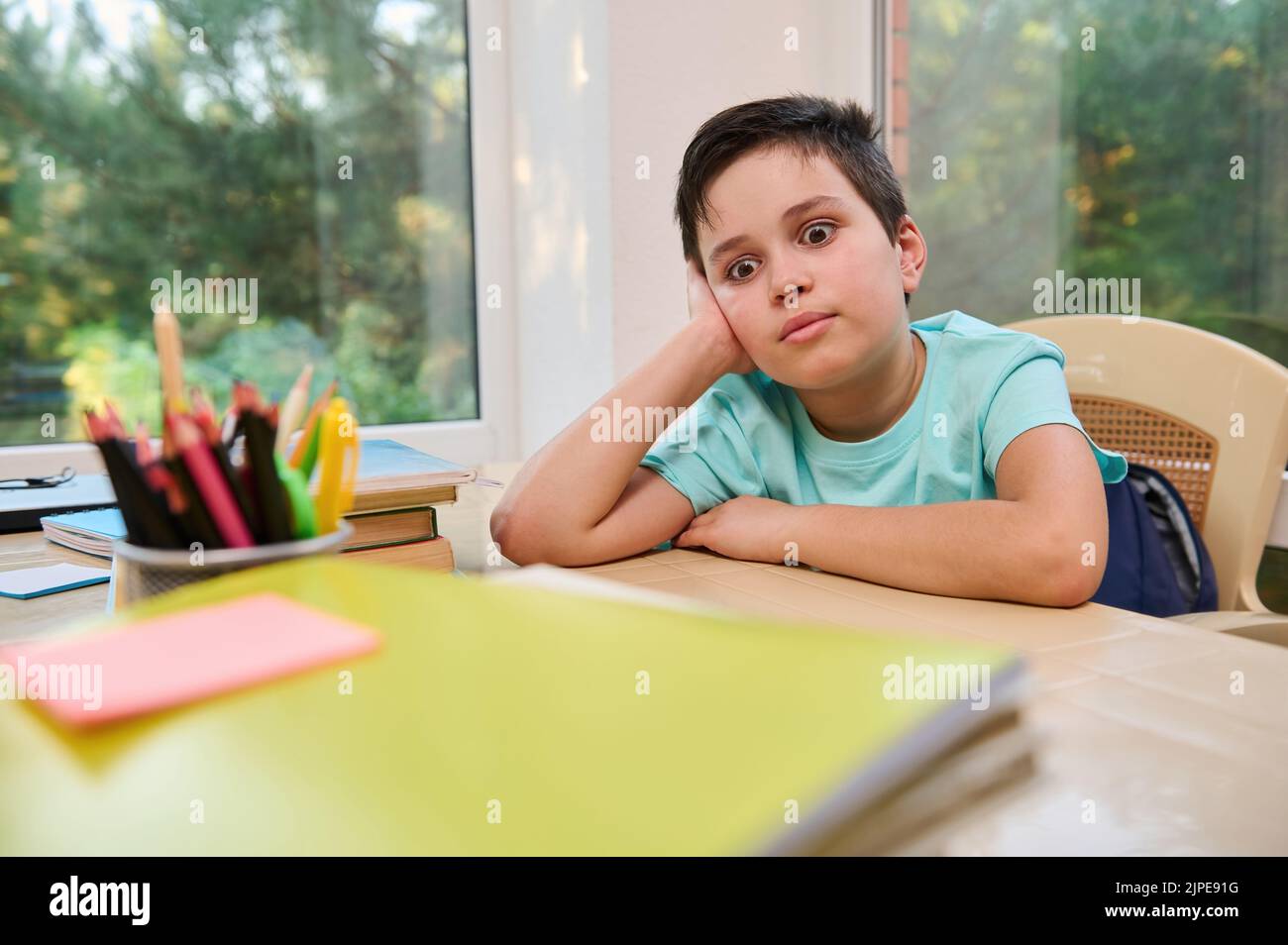 Un écolier ennuyé assis à son bureau, regardant de côté, ayant de la difficulté à s'adapter à un nouveau semestre d'année scolaire Banque D'Images