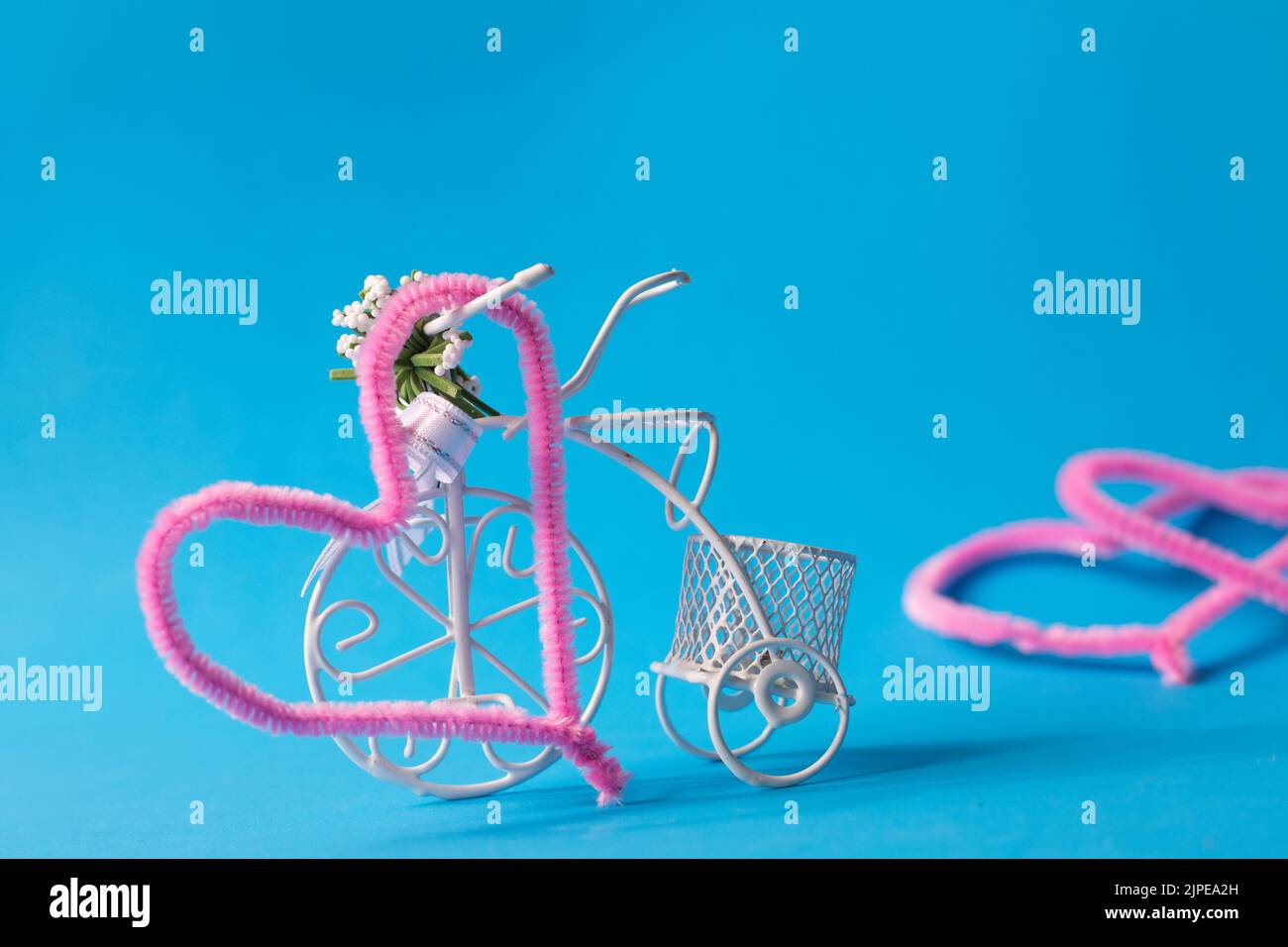 Vélo décoratif, figurine de vélo en fil blanc fin isolé sur fond bleu. Coeurs roses sur le dos. Laisser, métaphore de la séparation, allégorie. Banque D'Images
