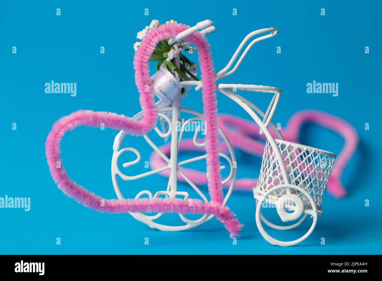Vélo décoratif, figurine de vélo en fil blanc fin isolé sur fond bleu. Coeurs roses sur le dos. Laisser, métaphore de la séparation, allégorie. Banque D'Images