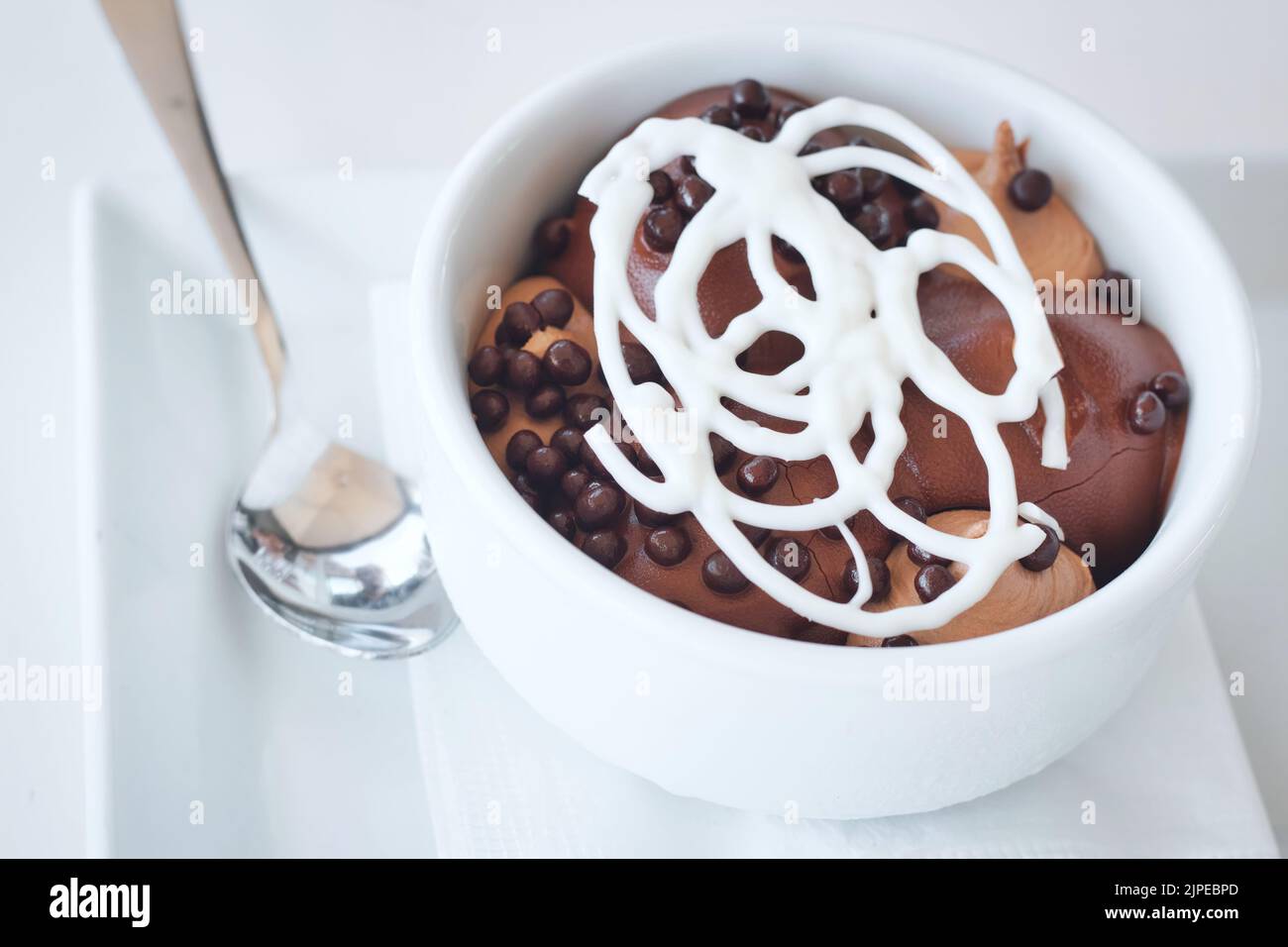 Profiteroles avec une garniture en treillis au chocolat blanc dans un bol en céramique blanc avec une cuillère en argent Banque D'Images