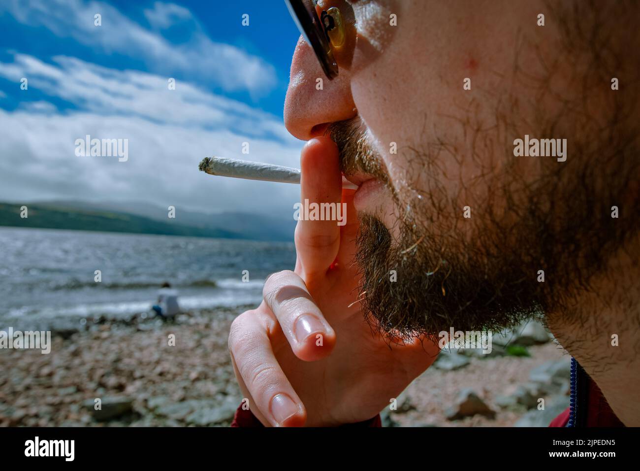 Détail d'un homme qui fume un joint de marijuana ou de mauvaise herbe se détendant sur la rive d'un lac. Banque D'Images