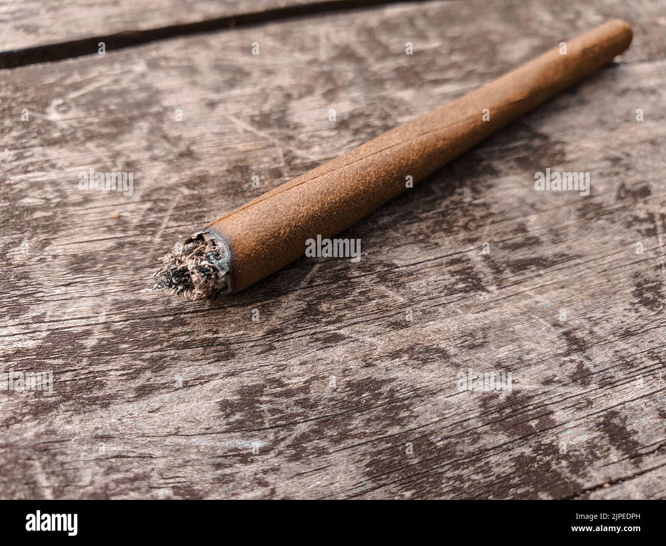 Détail d'un joint éclairé de marijuana ou de mauvaise herbe sur une table en bois marron à l'extérieur. Banque D'Images