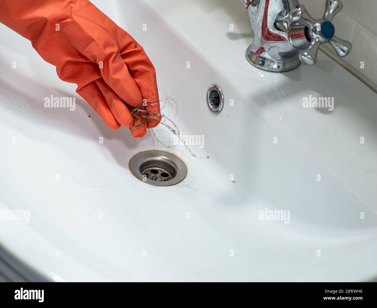 La main dans les gants orange retient beaucoup de perte de cheveux sur le filtre dans le lavabo pendant le nettoyage Banque D'Images