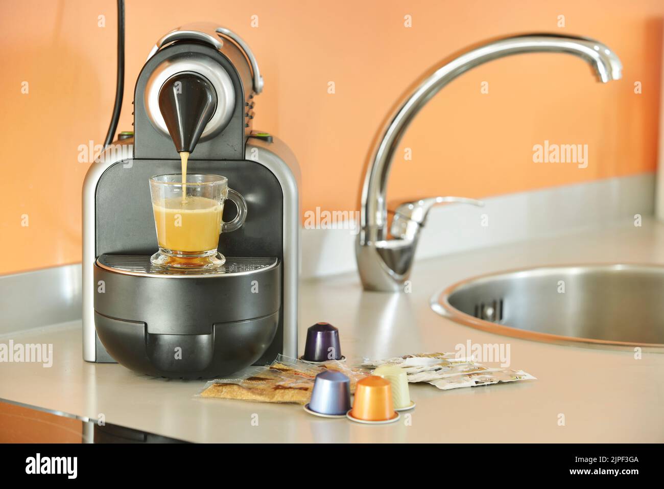 Préparation d'un café au lait dans une cuisine équipée d'une machine à café à capsule avec comptoir gris Banque D'Images