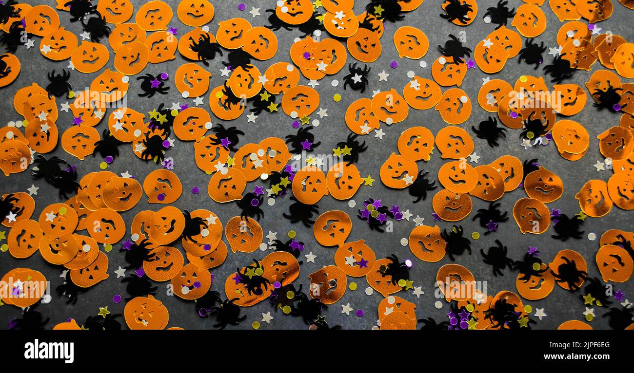 Arrière-plan Halloween : confetti brillants en forme de citrouilles orange, araignées noires et étoiles violettes dorées. Banque D'Images