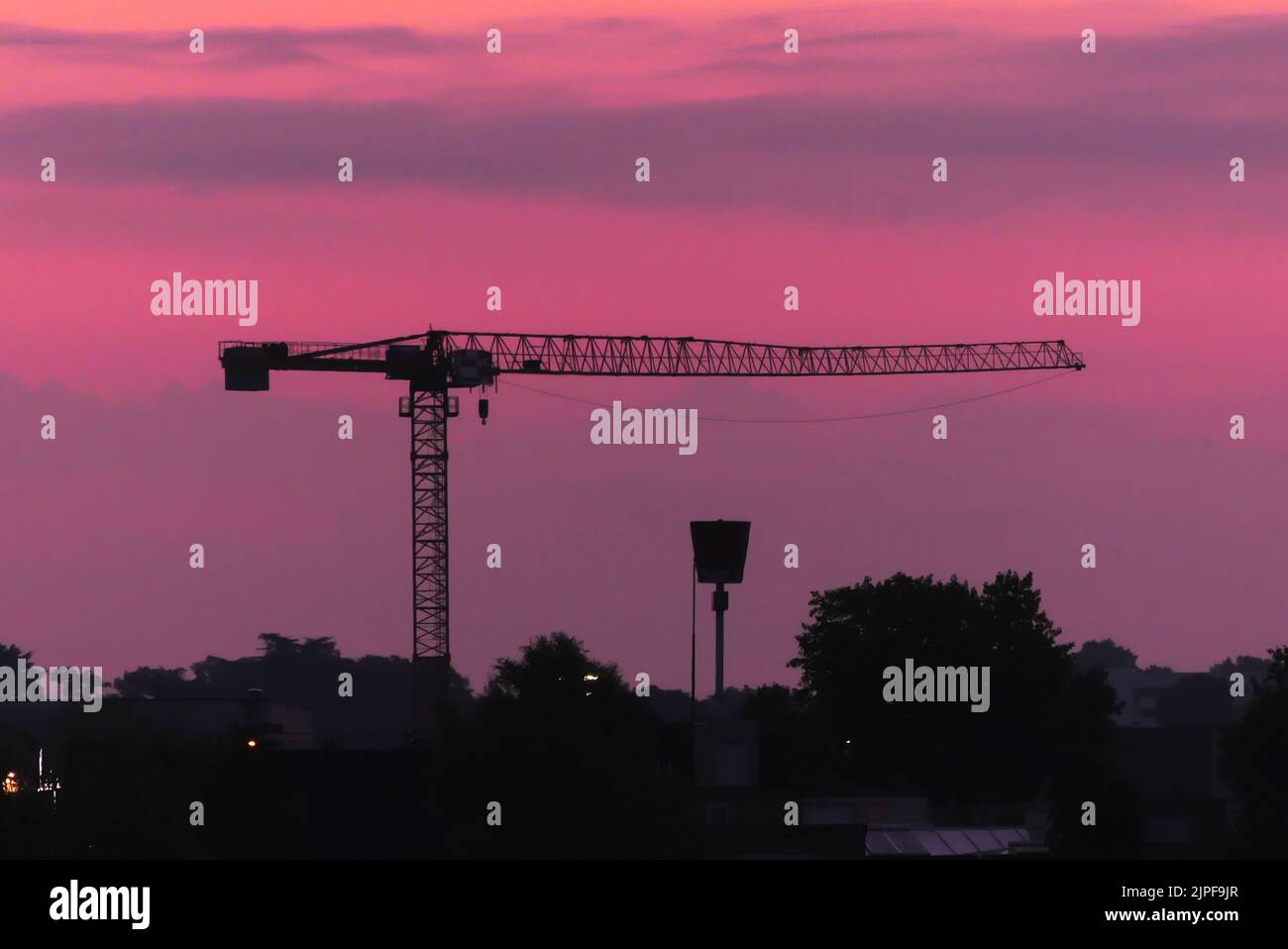 Vue sur la ville au lever ou au coucher du soleil avec le chantier de construction. Silhouette d'une grue de construction. Banque D'Images