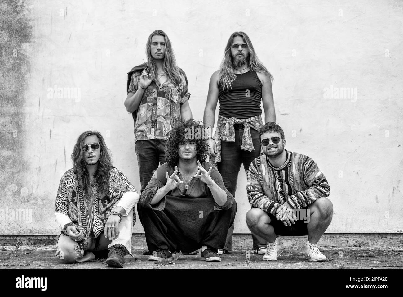 cinq hommes posent sur un fond blanc, trois agenouillement, deux debout, cheveux longs, groupe rock, musiciens Banque D'Images