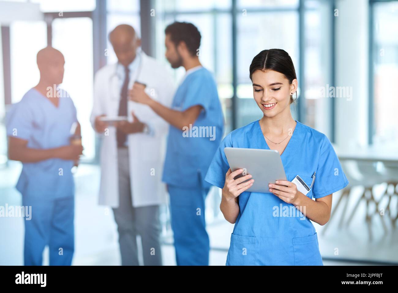 Un jeune médecin qui utilise une tablette numérique dans un hôpital avec ses collègues en arrière-plan. Banque D'Images