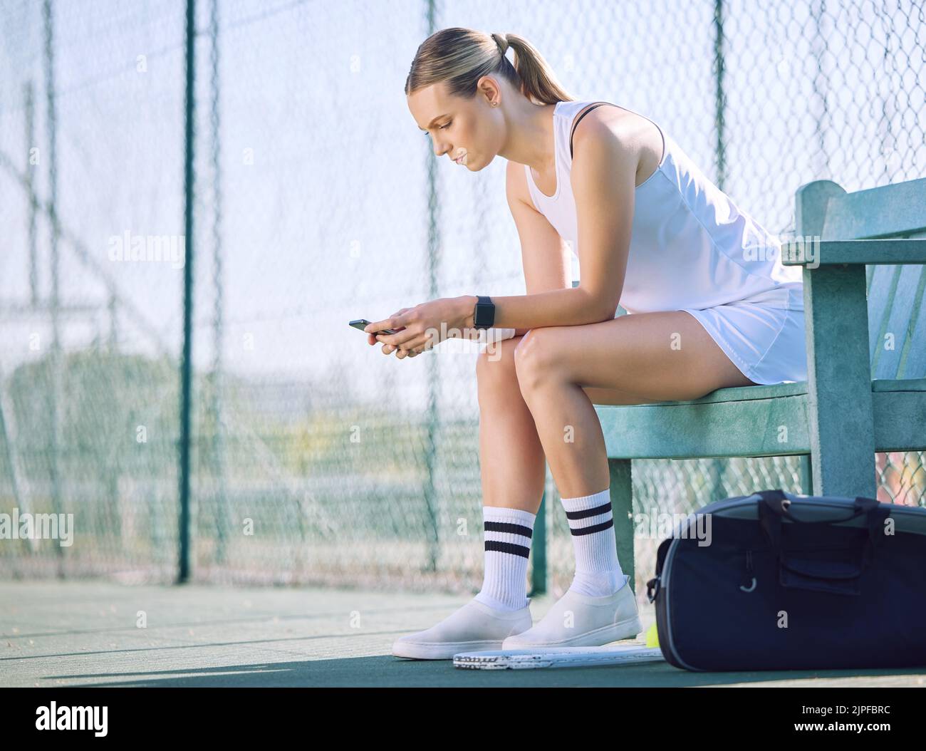 Une joueuse de tennis féminine avec un téléphone vérifiant la progression de l'objectif de fitness sur l'application d'exercice moderne en ligne tout en prenant une pause sur le court. Une femme sportive Banque D'Images