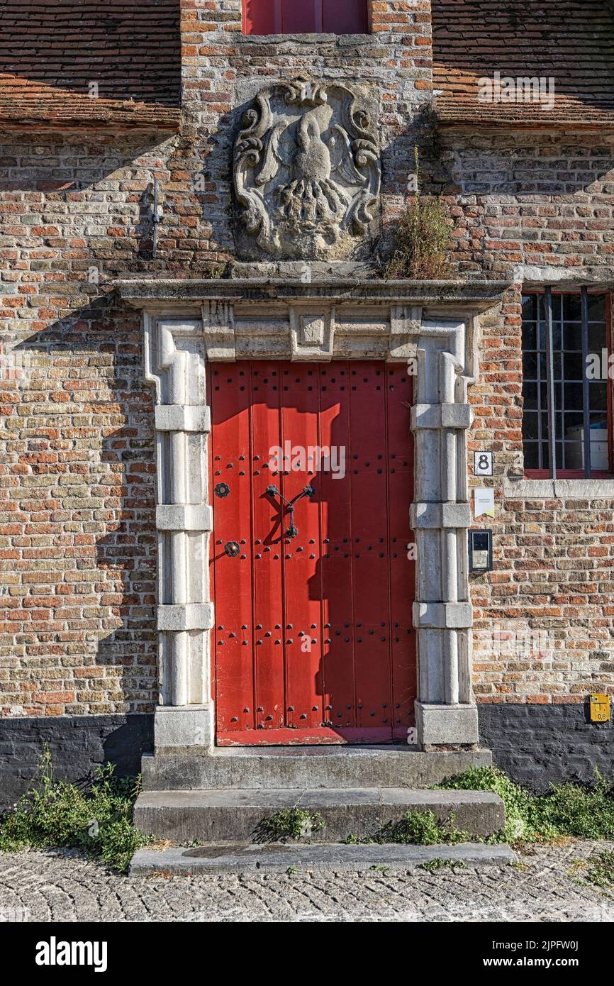 BRUGES, BELGIQUE - 11 AOÛT 2022 : porte rouge et cadre de porte en pierre sur un bâtiment médiéval dans le centre-ville Banque D'Images