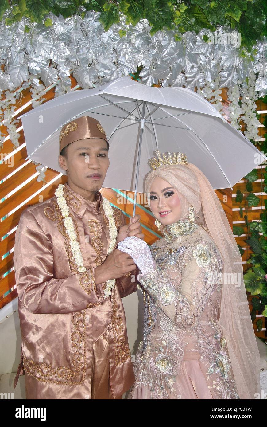 Tegal, INDONÉSIE - 22 décembre 2019 : la mariée et le marié en robes beiges posent à l'aide d'un parapluie. Banque D'Images