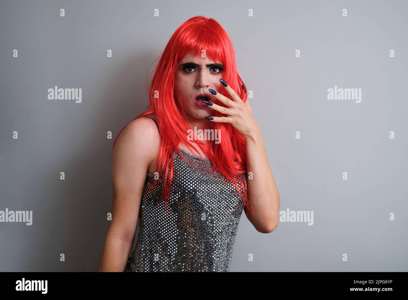 Portrait de la reine de drag étonné portant une perruque rouge et regardant l'appareil photo. Banque D'Images