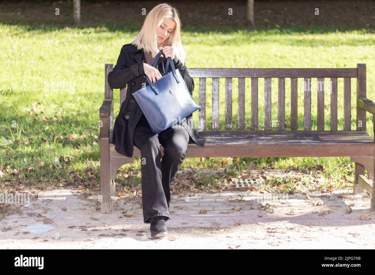 femme blonde assise sur un banc de parc vêtue de noir Banque D'Images