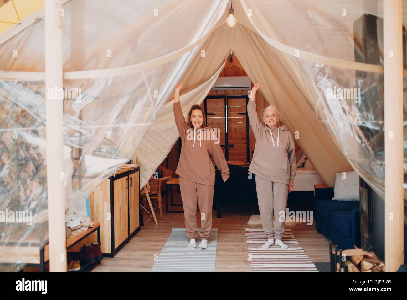Famille faire des exercices d'échauffement sports idoors. Jeune et âgée, femme se détendant dans une tente de camping glamping. Mère et fille moderne à la forme physique vacances concept de style de vie Banque D'Images