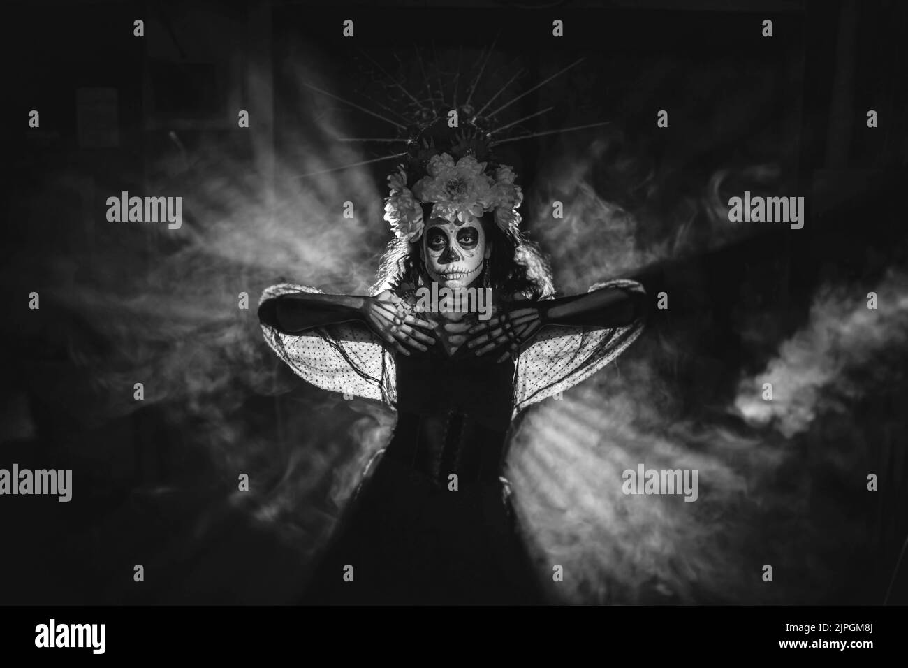 Femme avec le crâne mexicain halloween maquillage dans l'obscurité avec des rayons de contre-jour. Jour des morts alias Dia de los Muertos et halloween concept noir et blanc. Banque D'Images