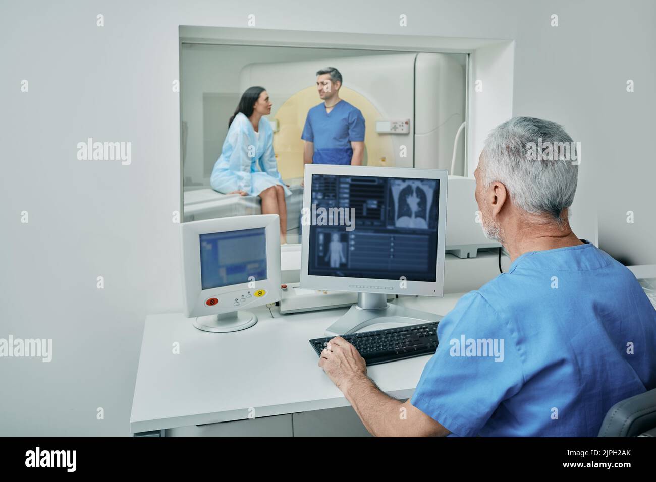 Médecin radiologue attendant dans la salle de contrôle derrière le verre de protection pendant que l'assistant médical prépare la patiente pour la tomodensitométrie. Tomodensitométrie s Banque D'Images