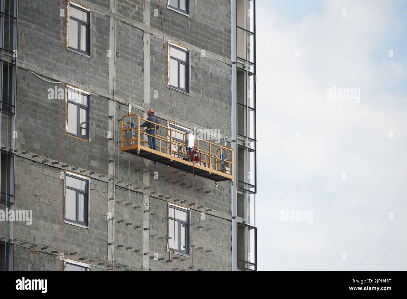 Builder travaille dans une plate-forme suspendue spéciale à la construction d'un immeuble d'appartements Banque D'Images