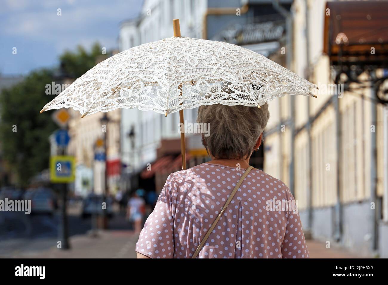 Vieille femme avec parasol marcher sur une rue sur le fond des gens. Temps chaud, vie des personnes âgées en été Banque D'Images