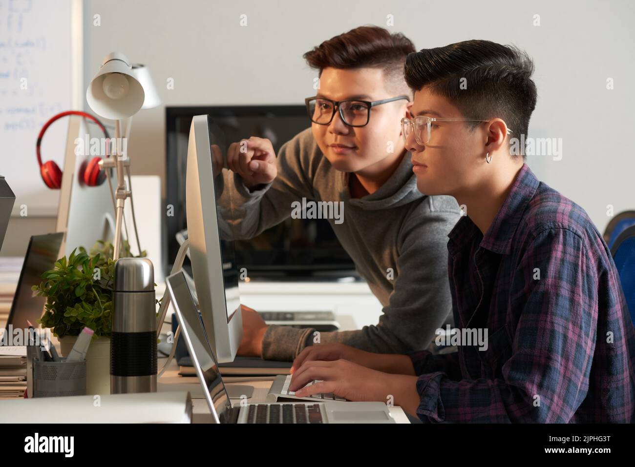 Groupe de jeunes cadres talentueux en vêtements décontractés réunis devant un ordinateur moderne et travaillant sur un projet de démarrage, à l'intérieur d'un bureau ouvert en arrière-plan Banque D'Images